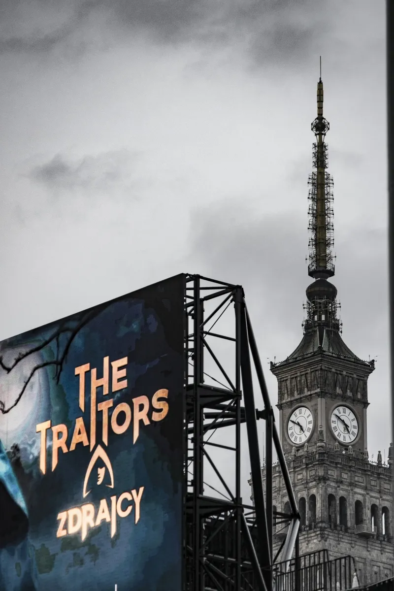 Palace of Culture and Science clock tower beside a billboard for The Traitors